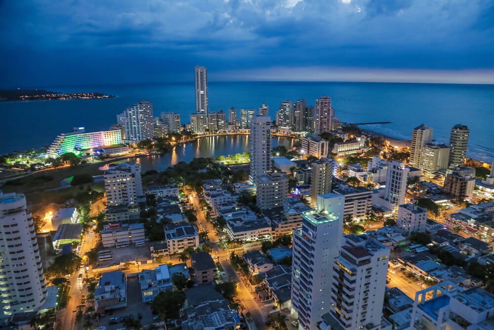 Vista noturna e aérea de Bocagrande, em Cartagena. Há muitos prédios e ruas iluminadas. O mar está na parte de trás do cenário.