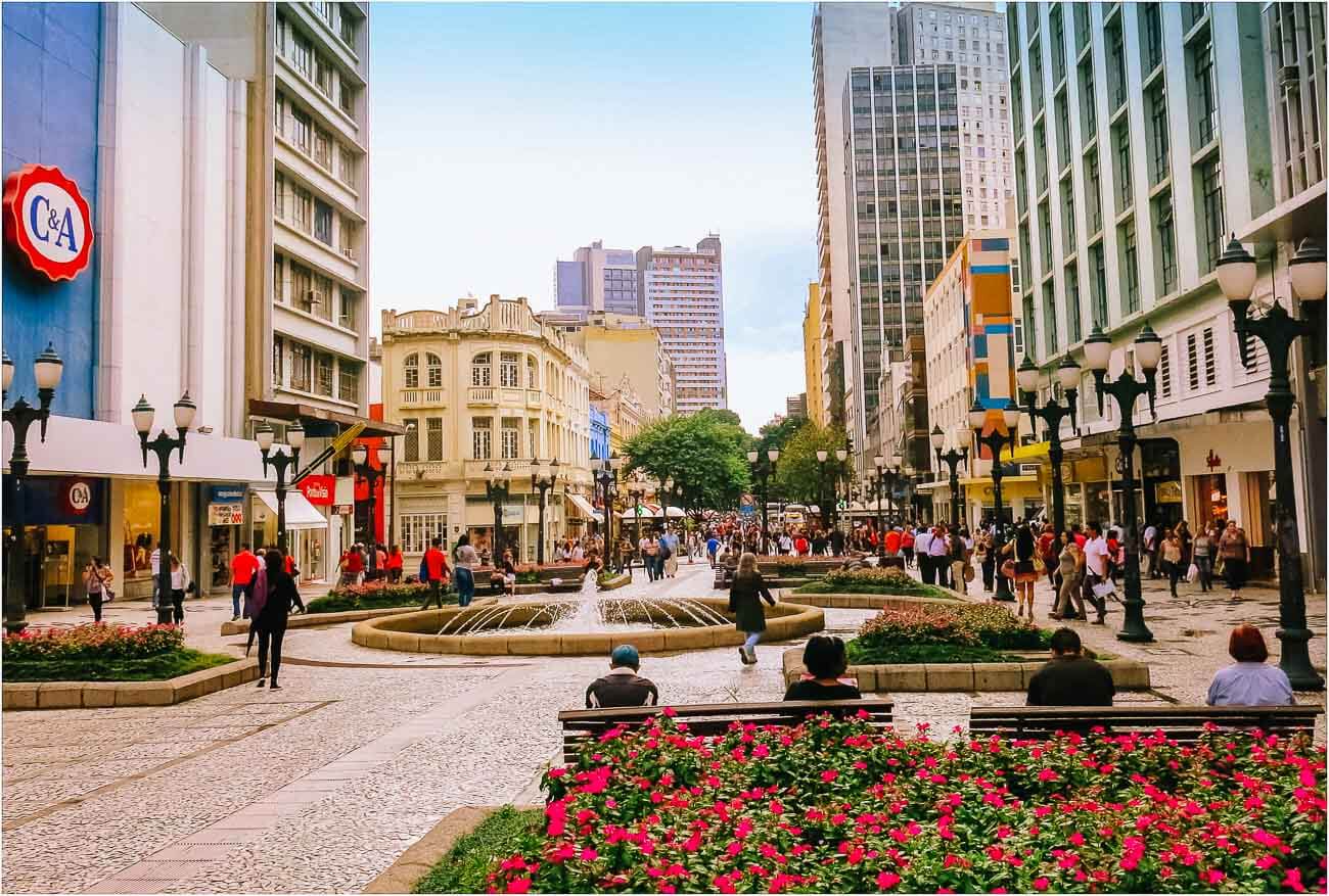Centro de Curitiba com algumas pessoas caminhando e vários canteiros de flores.
