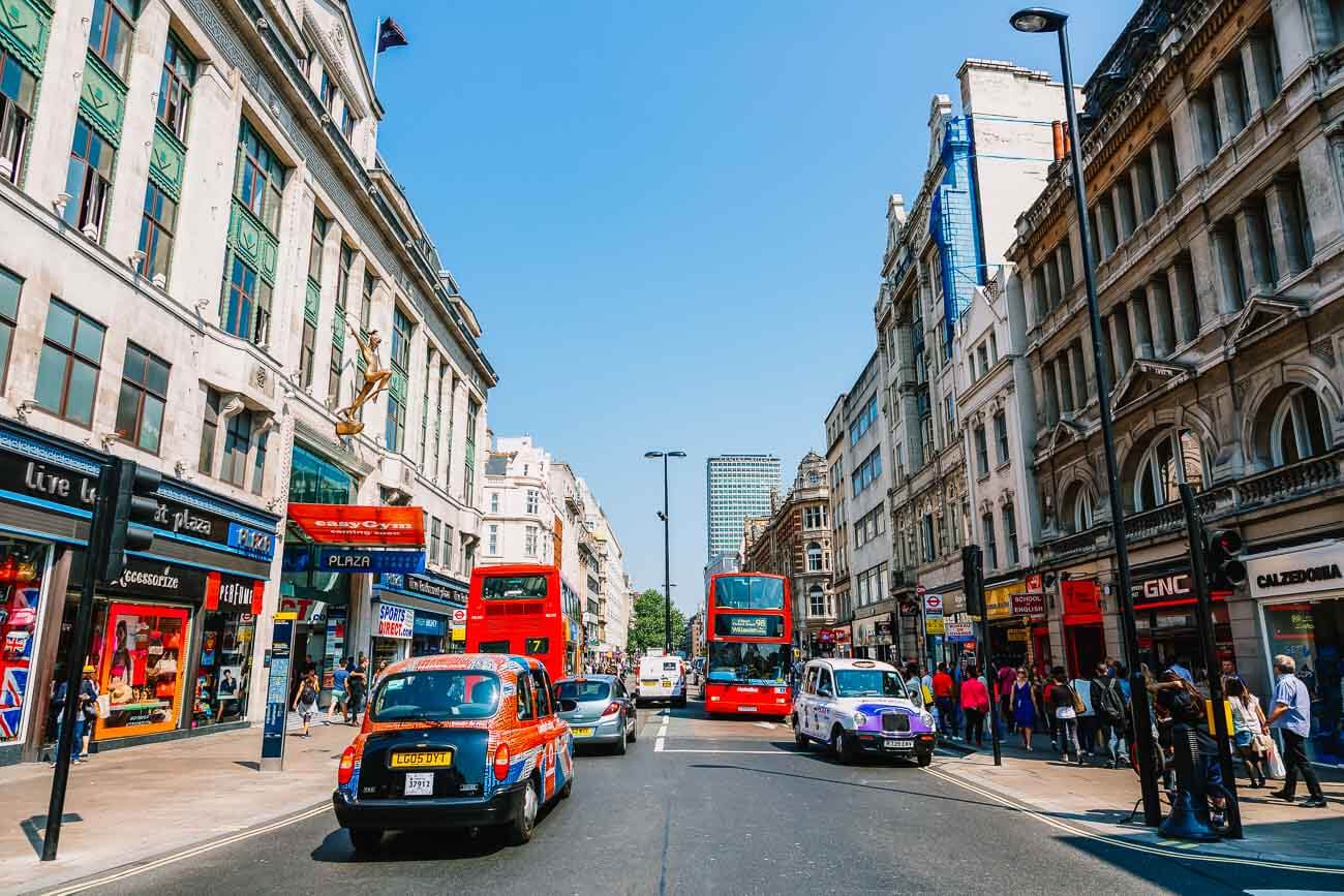 Rua Oxford em Londres com carros e ônibus vermelhos. Nas calçadas, pessoas caminhando.