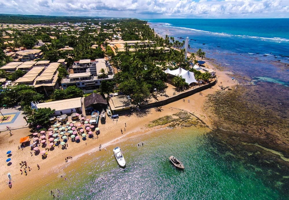 Vista aérea da Praia do Forte com águas esverdeadas e banhistas na areia.