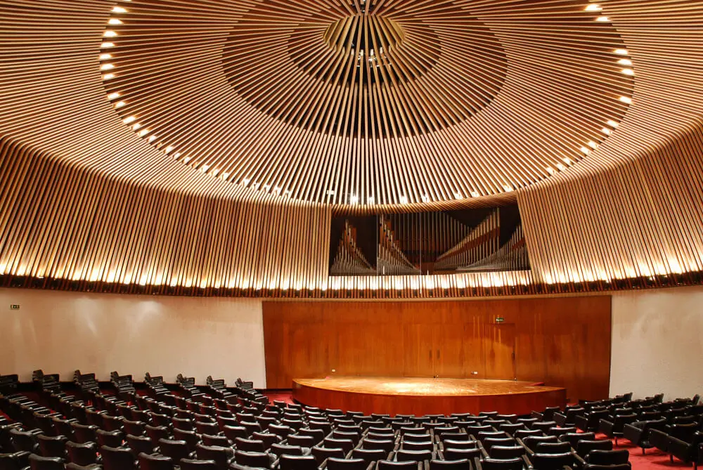 Sala de concertos da Biblioteca Luis Ángel Arango, em Bogotá. Há muitas cadeiras na plateia e um palco de madeira.