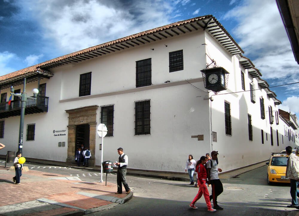 Frente do Museo Casa de La Moneda com paredes brancas e pessoas caminhando pela rua em frente ao local.