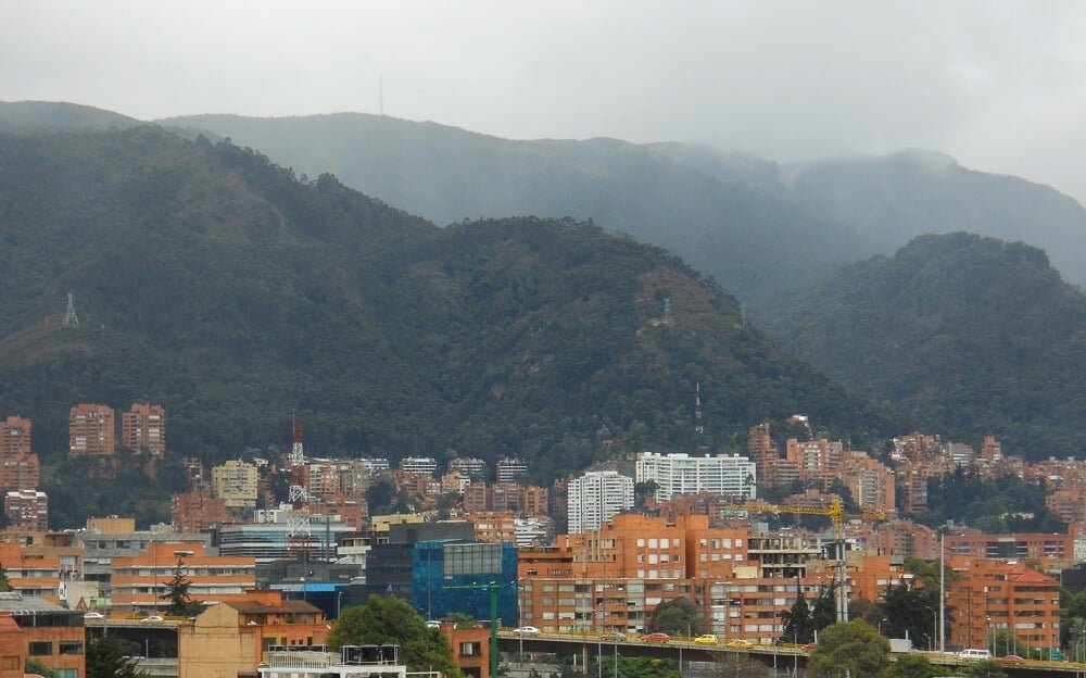 Bairro Chapinero visto de cima em um dia nublado. Há muitos prédios e montes cobertos pela vegetação.