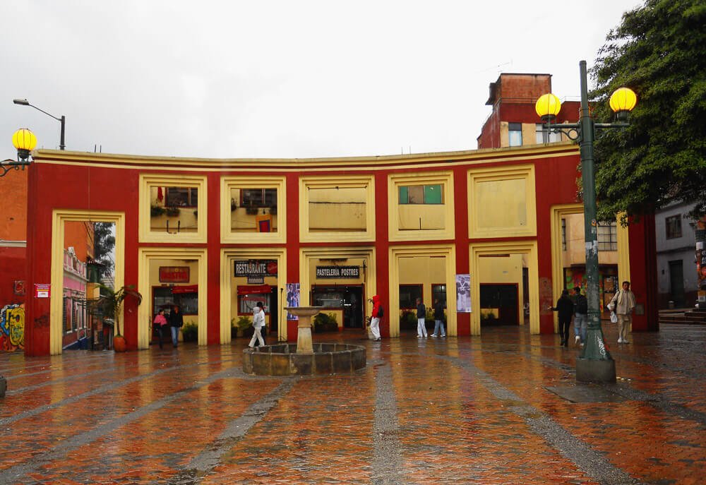 Plazoleta Chorro de Quevedo com piso amarronzado e edifício amarelo e vermelho.