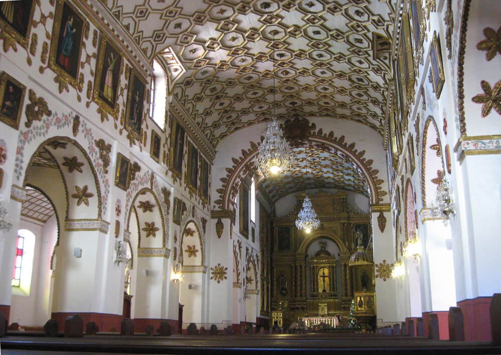 Interior da La Iglesia de San Agustín com muitos bancos de madeira, altar dourado e decoração no teto.