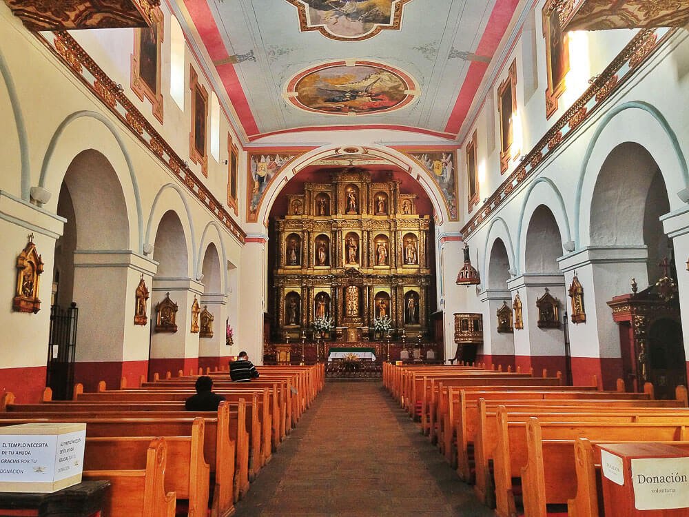 Interior da Iglesia de la Candelaria com bancos laranja, altar com muito ouro e pinturas no teto.