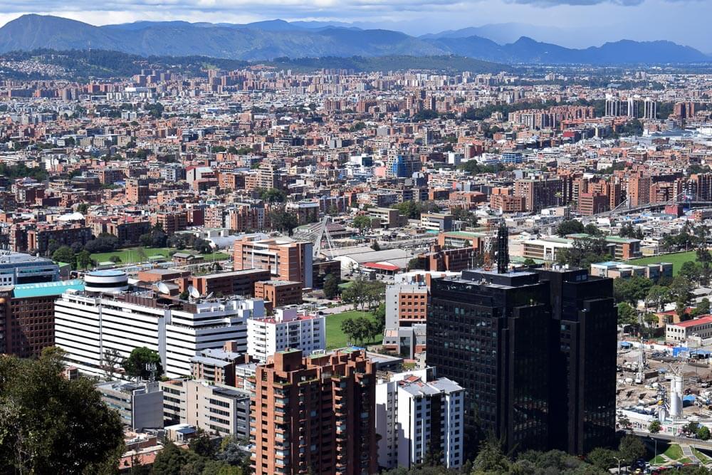 Visão aérea de Bogotá com muitos prédios. Há montanhas ao fundo.