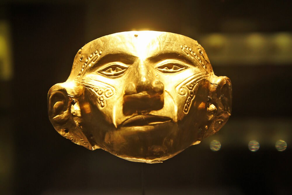 Peça de ouro em formato de máscara antiga.