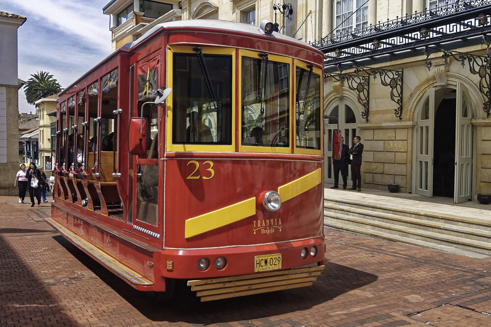 Trem antigo de Bogotá, vermelho com detalhes amarelos, exposto em uma rua com prédios claros.