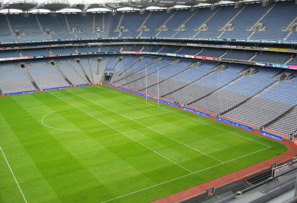 Estádio Croke Park. Há um extenso campo de futebol e uma arquibancada azul.