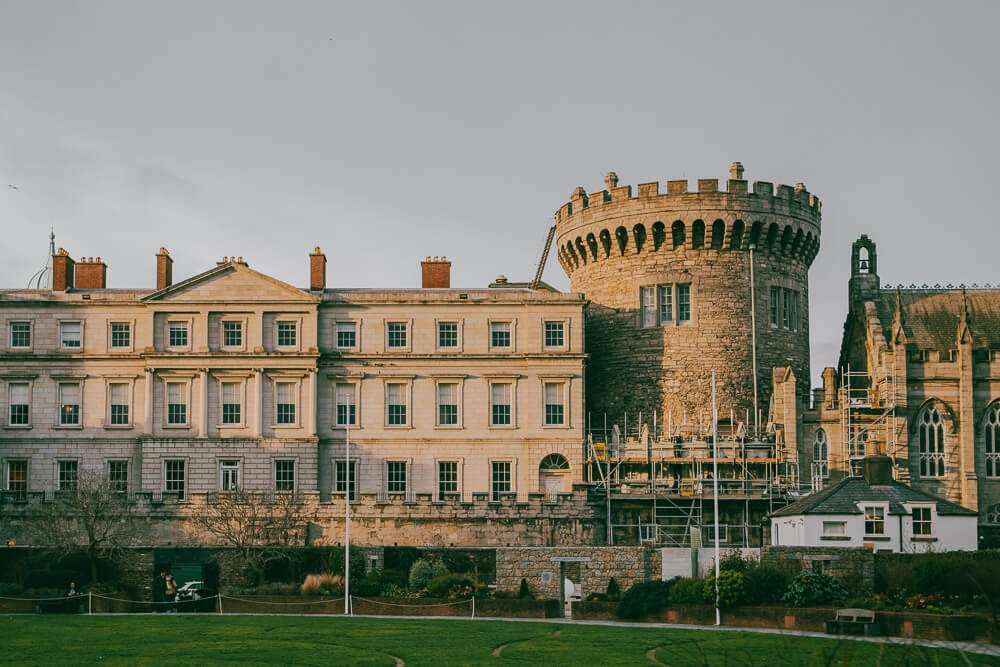 Dublin castle com paredes e torre em tons de areia e um jardim em frente.