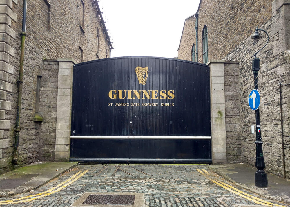 Portão frontal do Guinness Storehouse. Há paredes de pedra nas laterais do portão azul escuro.