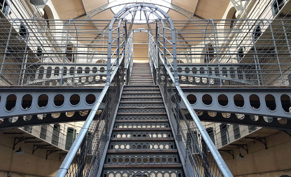 Escadaria interior da Kilmainham Gaol. No centro, há uma escada feita de metal.