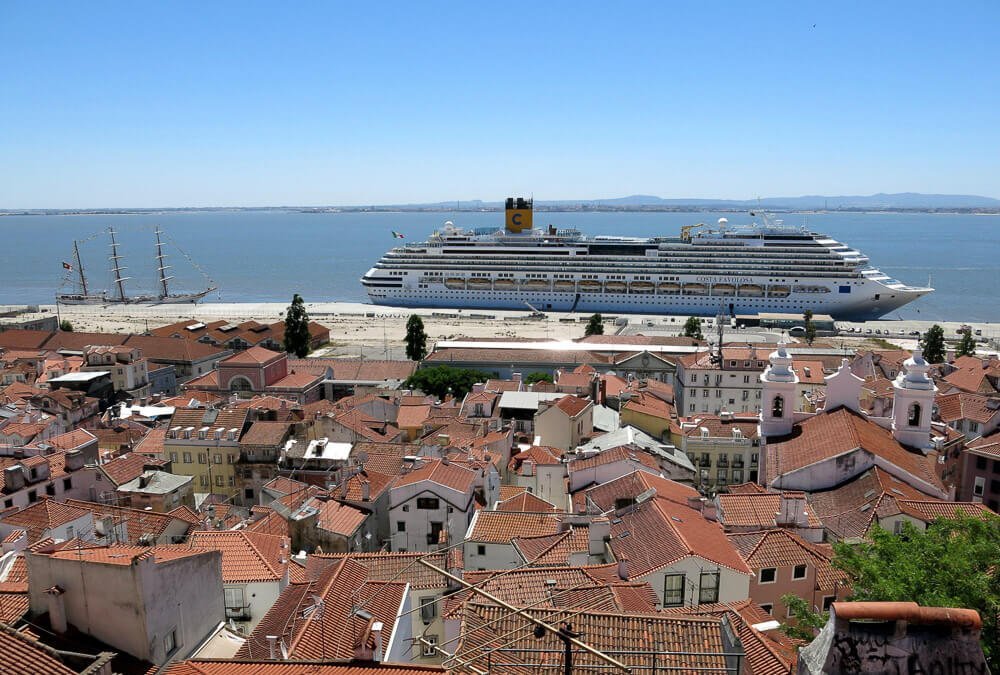 Casas e cruzeiro vistos de cima. Há um grande navio branco sobre as águas azuis do porto de Lisboa.