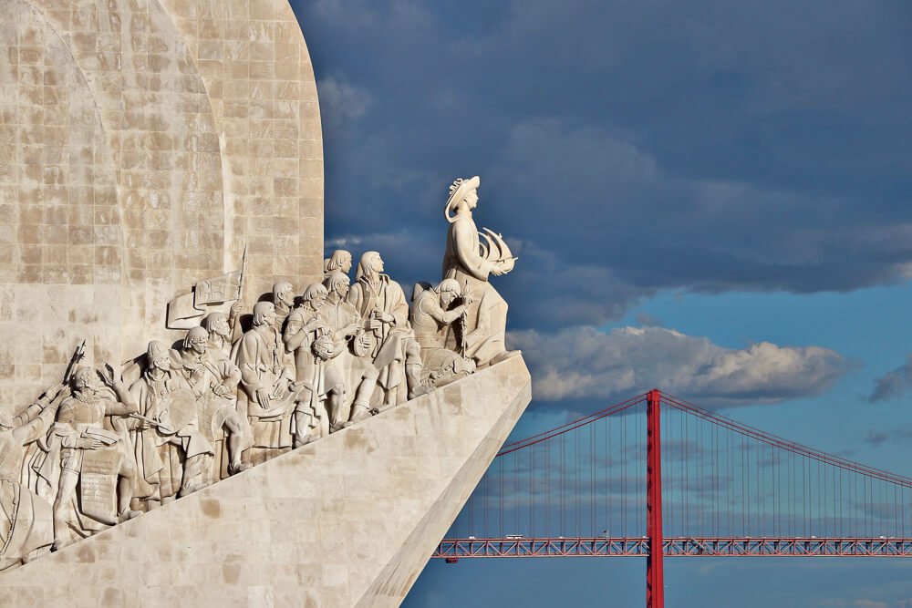 Esculturas em tons de areia do Padrão dos Descobrimentos e, ao lado, a Ponte 25 de Abril, em Lisboa.