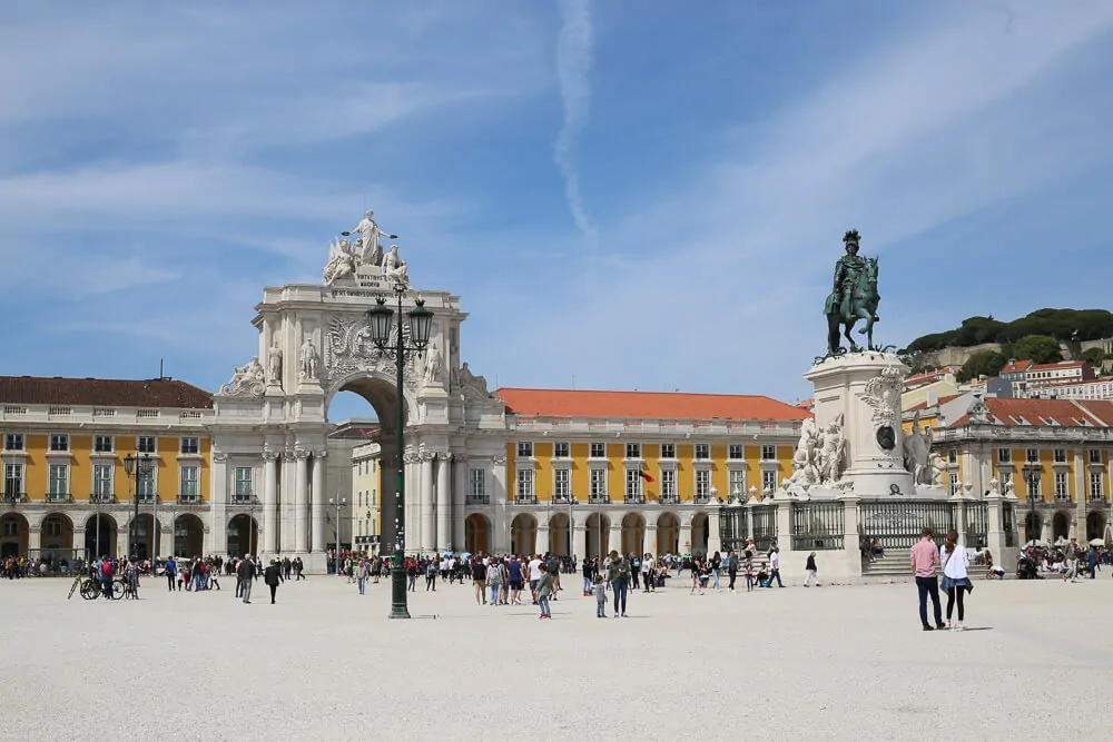 Praça do Comércio com arco Triunfal da Rua Augusta à esquerda. Há muitas pessoas no local.