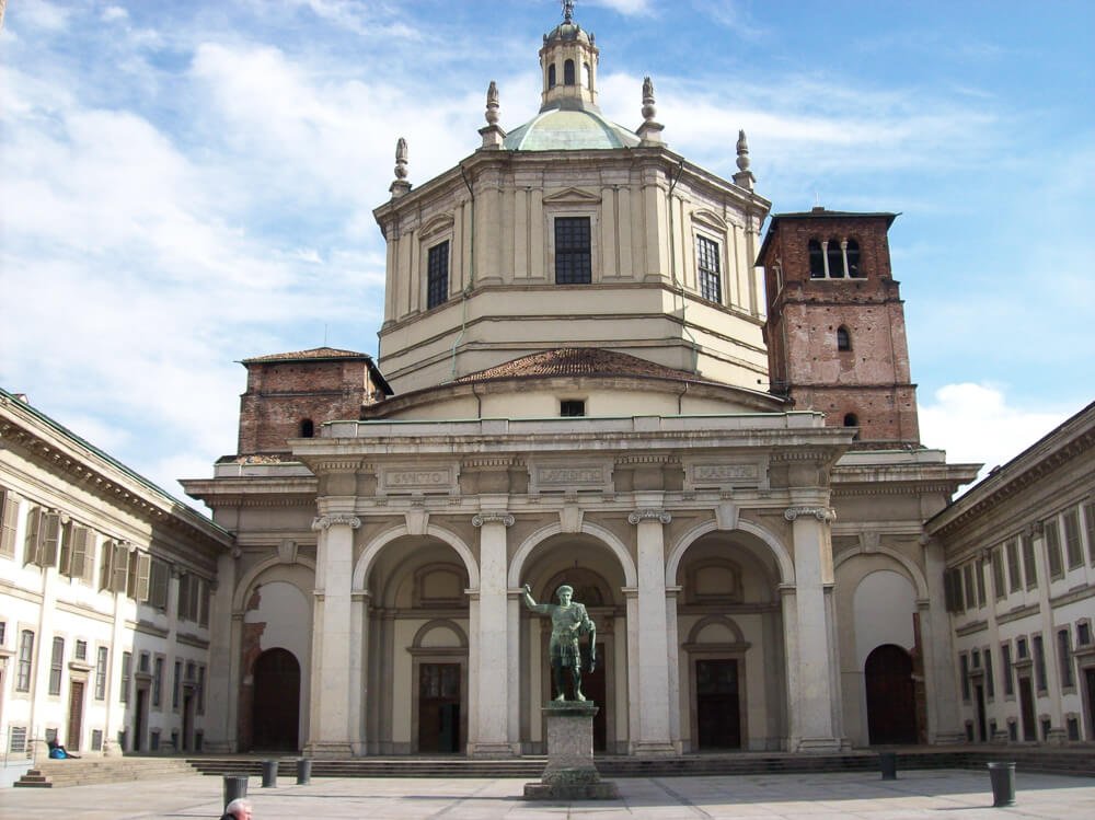 Fachada da Igreja de San Lorenzo Maggiore, em Milão. Há uma estátua masculina em frente ao prédio religioso.