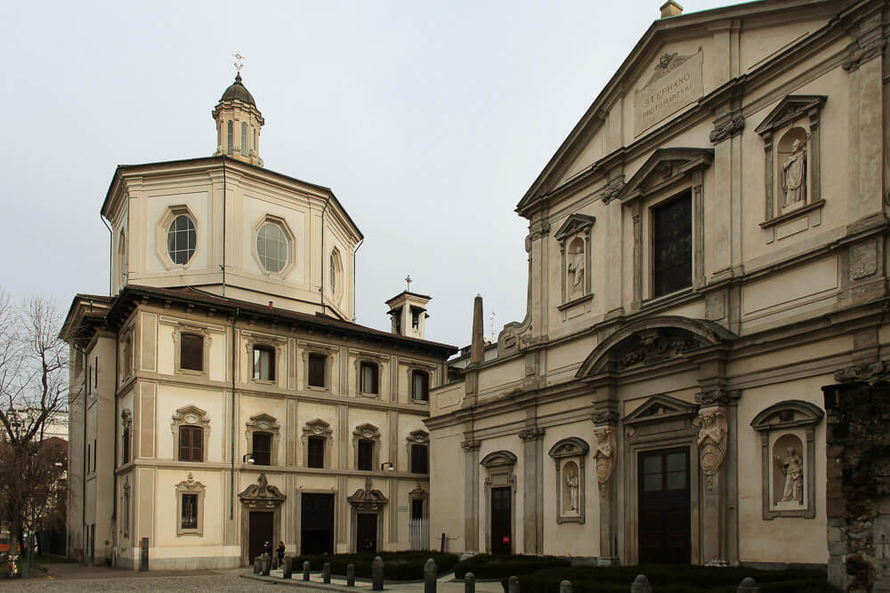 Parte externa da Igreja de San Bernardino alle Ossa com paredes claras e muitas janelas.