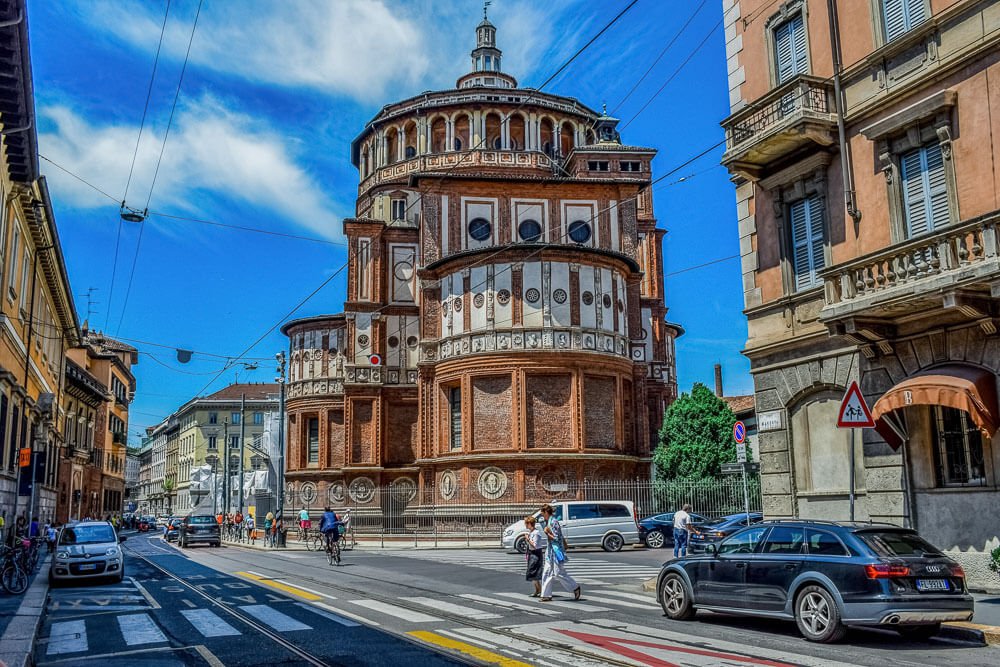 Torre da Igreja de Santa Maria delle Grazie. Há uma rua com pessoas, carros e prédios à esquerda.