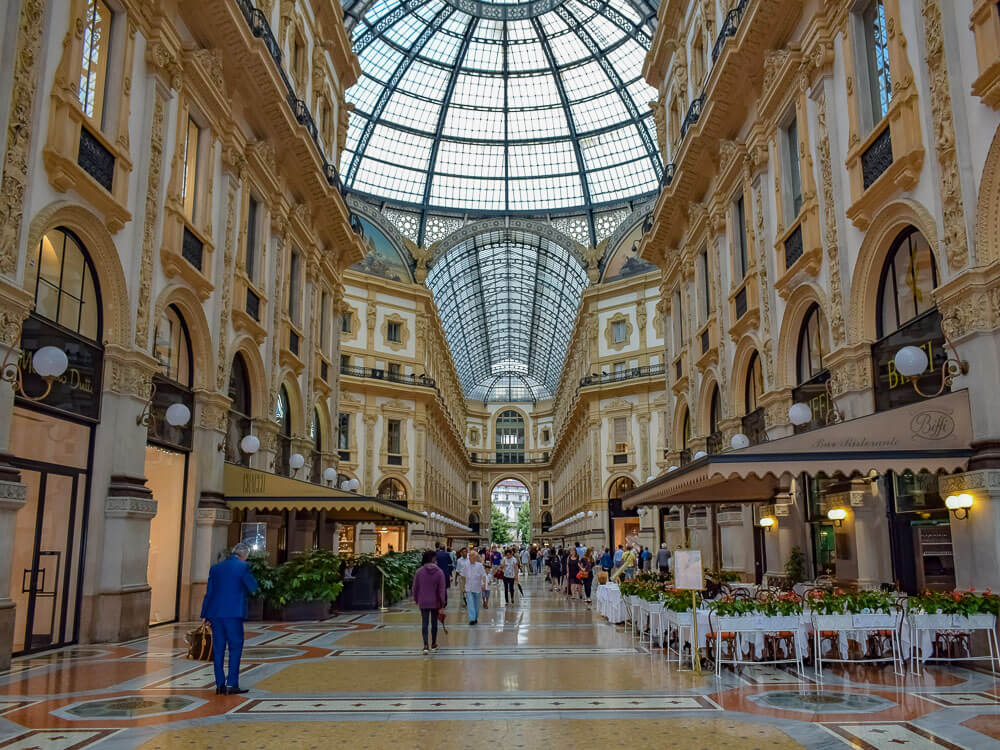 Interior da Galeria Vittorio Emanuelle II com restaurantes no térreo e teto de vidro.