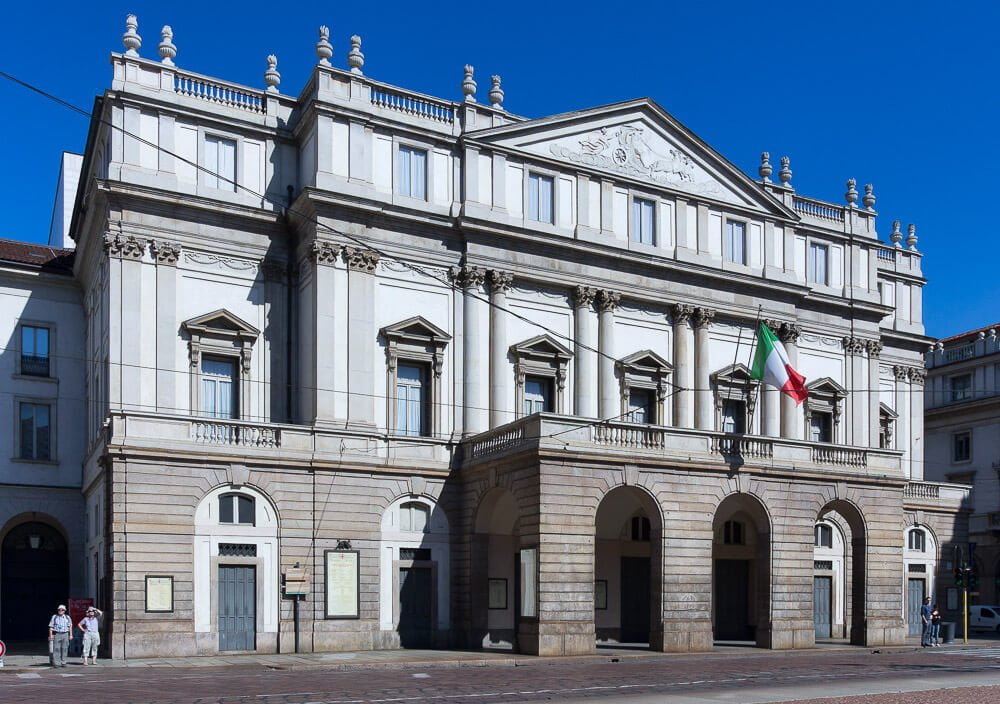 Fachada do Teatro alla Scala com bandeira da Itália hasteada em frente.