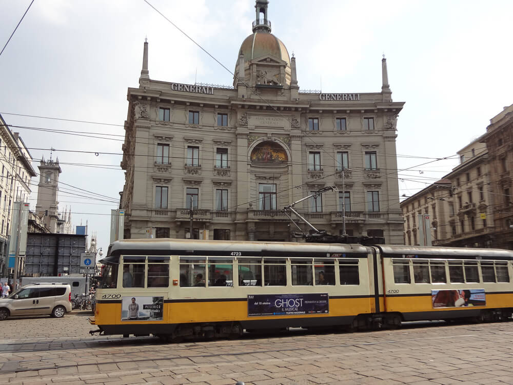 Trem amarelo passando por rua em Milão.