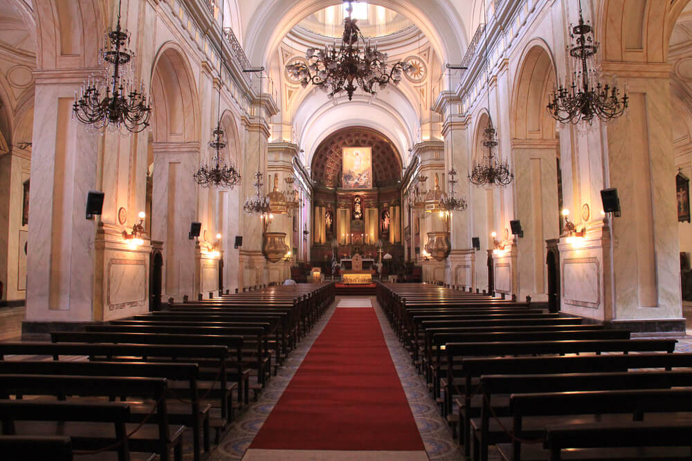 Interior da Catedral Metropolitana de Montevidéu. Há muitos bancos nas laterais e um tapete vermelho até o altar no centro.