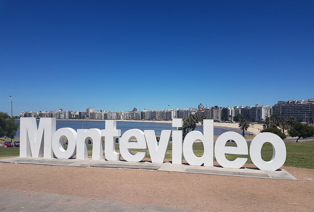 Letreiro de Montevidéu e, atrás dele, uma praia.