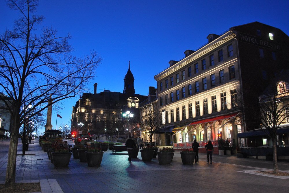 Place Jacques-Cartier durante a noite. Há prédios pouco iluminados e pessoas caminhando pelo local.