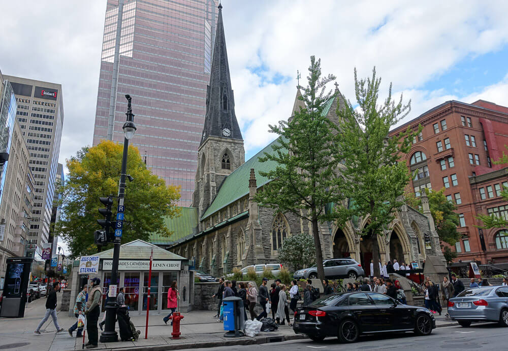 Rua Sainte Catherine com muitos prédios e uma igreja à direita. Há muitas pessoas caminhando pela calçada.