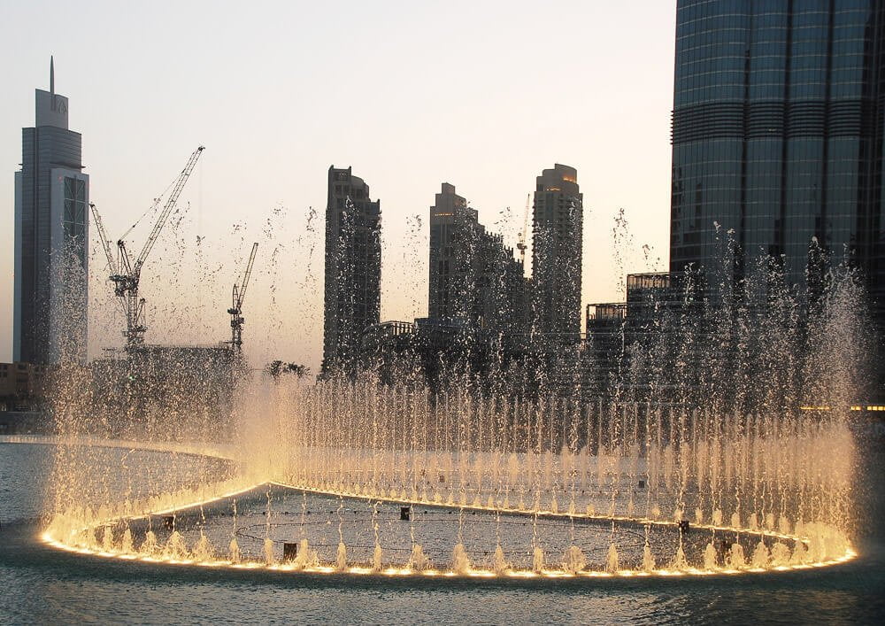 Fonte de Dubai em um fim de tarde. Há a silhueta de prédios ao fundo.