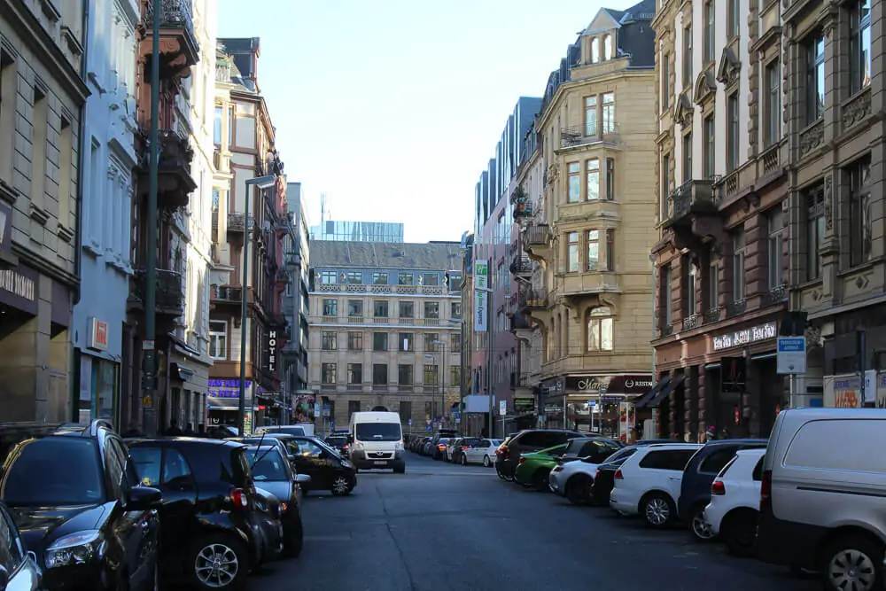 Rua em Bahnhofsviertel com vários prédios de arquitetura clássica europeia e carros estacionados.