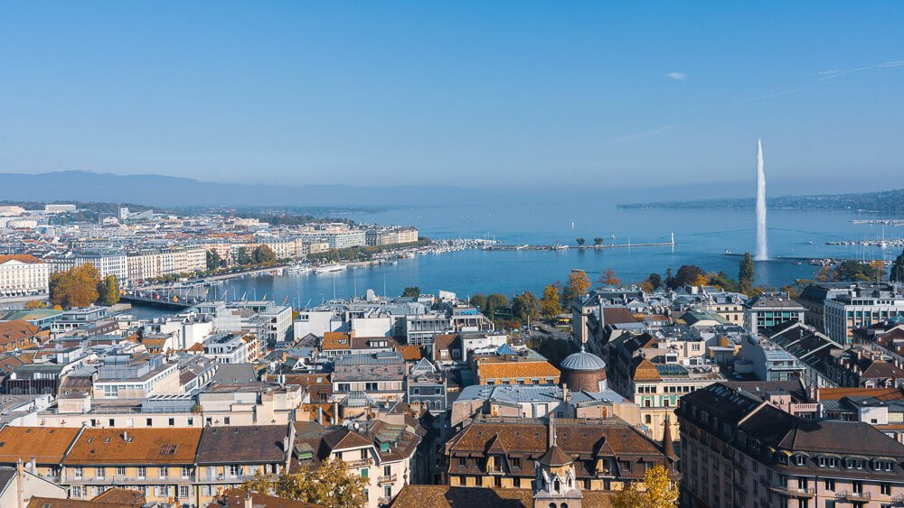Visão aérea da cidade de Genebra. Há o topo de muitos prédios tradicionais e, ao fundo, o Lago Léman e a fonte Jet d'Eau.