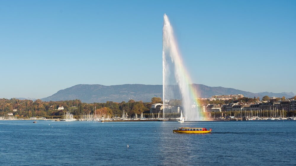 Lago Léman e fonte Jet d'Eau. Há árvores na região costeira.