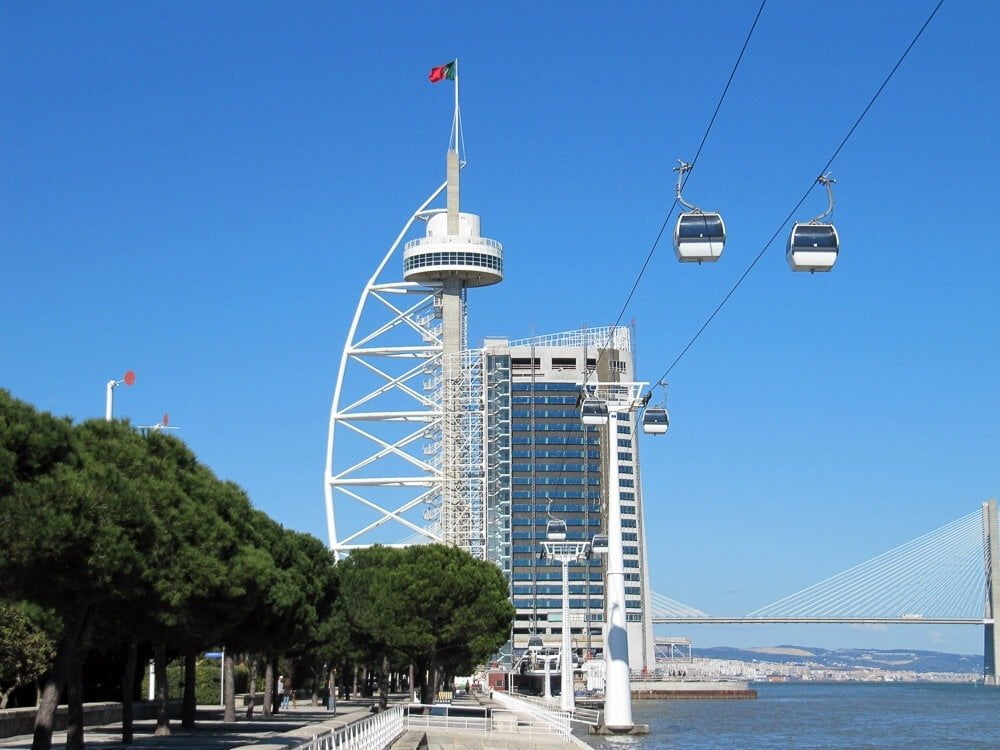 Teleférico no Parque das Nações. Ao fundo, um rio e um prédio moderno.