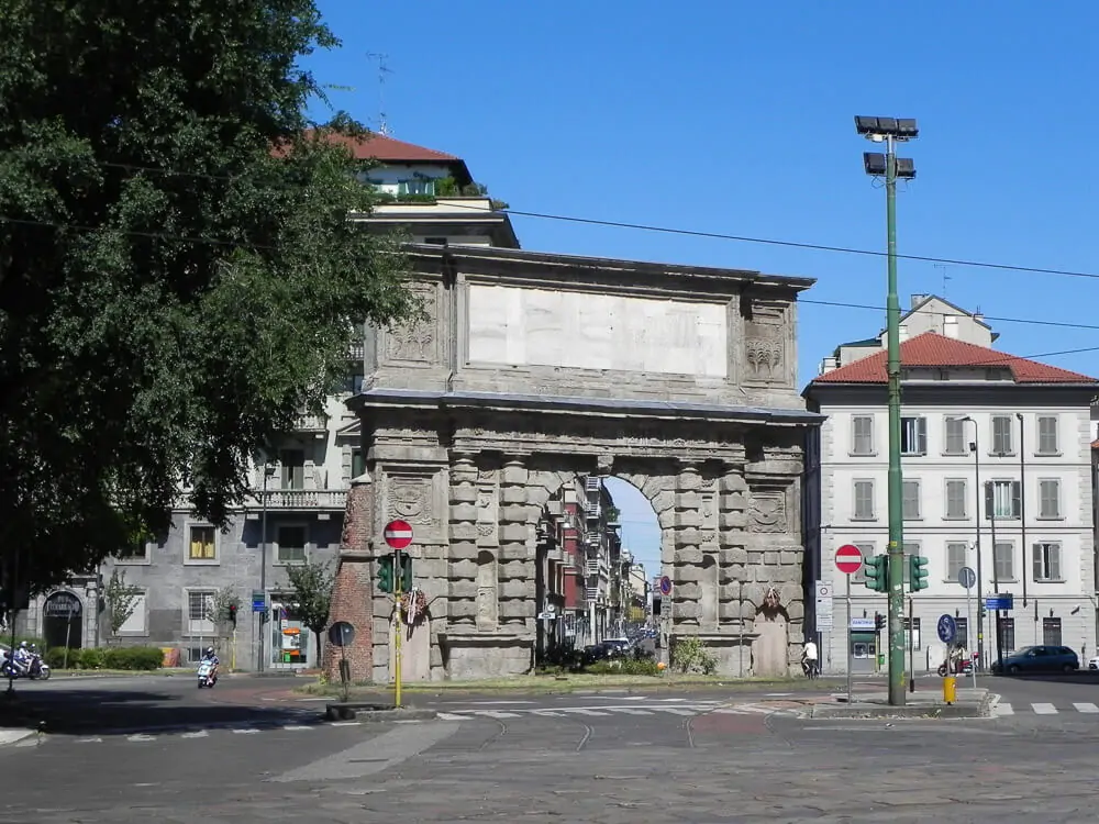 Arco em rua de Porta Romana. Há vários prédios de fachada clara e repletos de janelas ao fundo do arco.