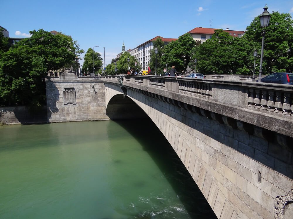 Ponte sobre Rio Isar em Au-Haidhausen. Há um rio de águas esverdeadas à esquerda e uma ponte cinza à direita.