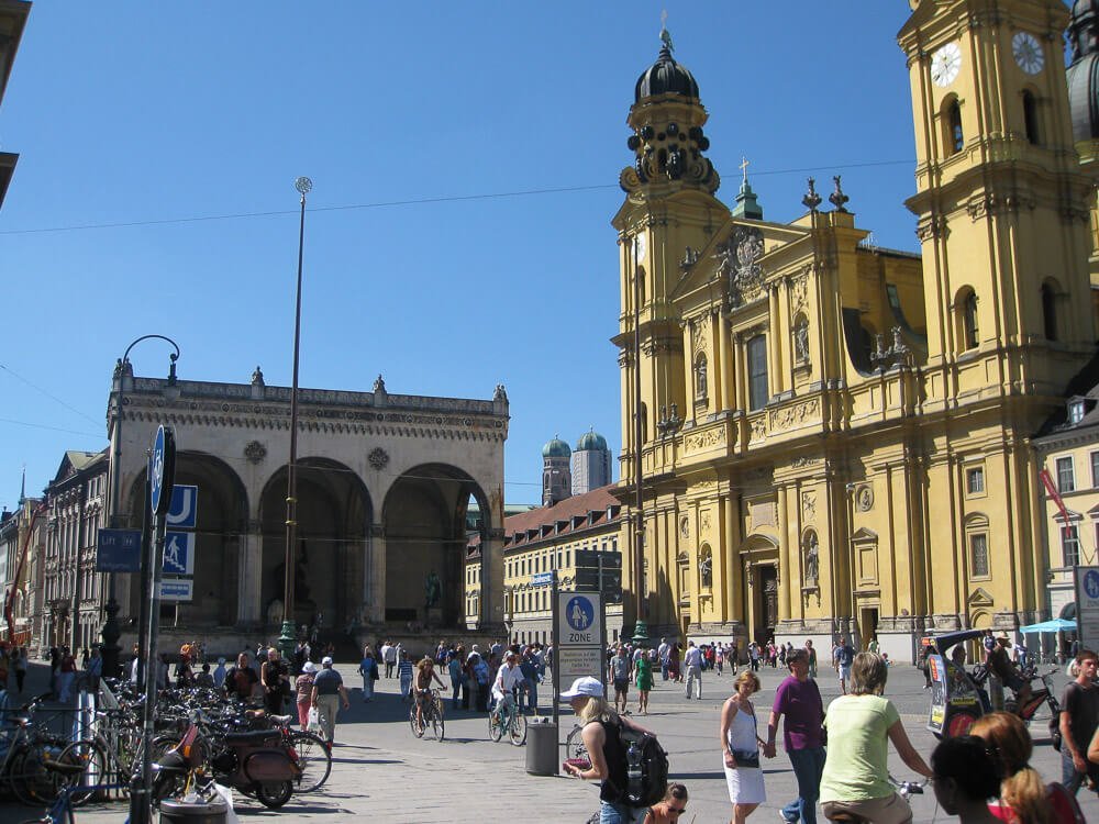 Praça Odeonsplatz com prédios históricos e muitas pessoas circulando pelo local.