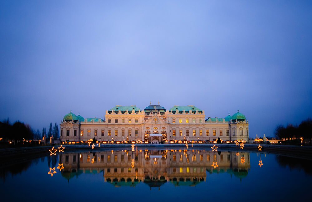 Palácio Belvedere iluminado em um fim de tarde e o lago do local refletindo o palácio.