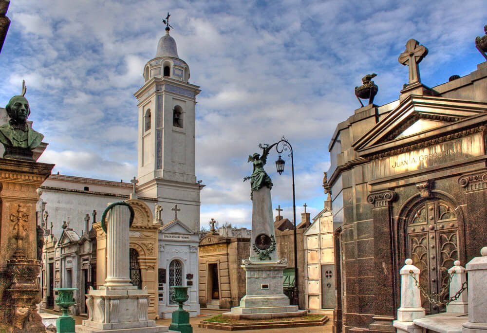 Interior do Cemitério da Recoleta com vários túmulos, estátuas e uma capela.