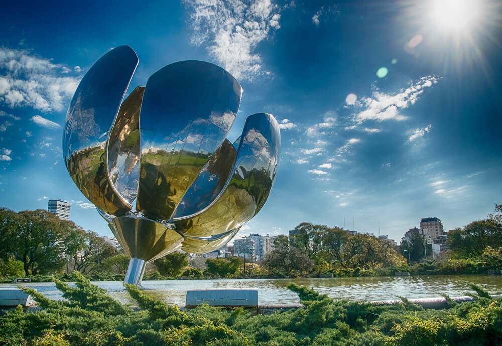 Escultura Floralis Generica em formato de flor, sobre um espelho d'água rodeado pela vegetação da região.