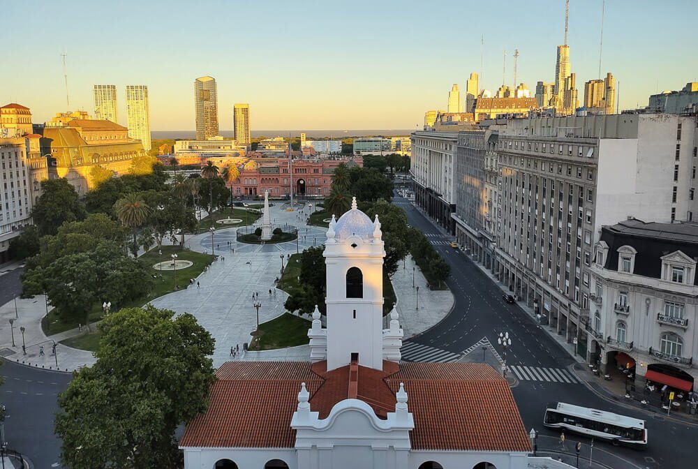 Visão superior da Praça de Maio com muitas árvores, prédios, a Casa Rosada e o Cabildo de Buenos Aires.