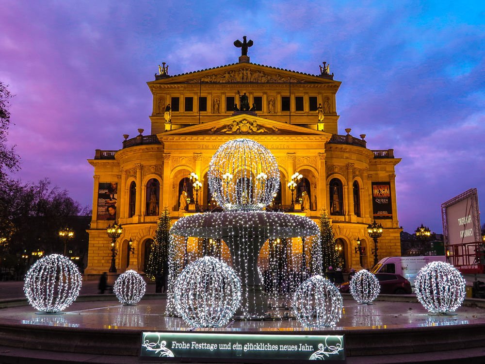 Fachada do prédio da Ópera de Frankfurt com uma fonte iluminada na frente.