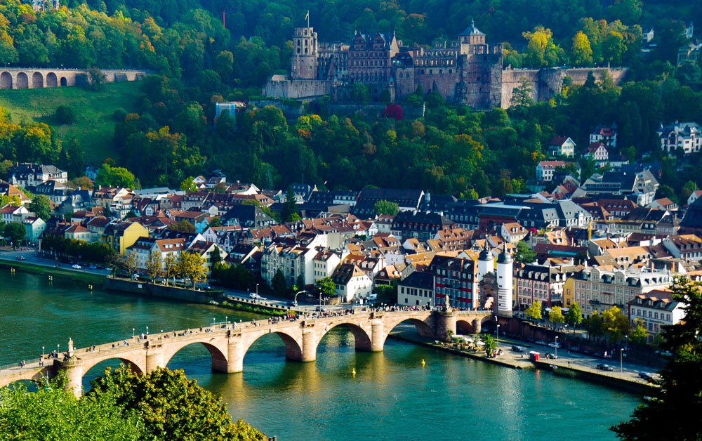 Cidade de Heidelberg vista de cima, com uma ponte sobre um rio de águas claras e vários prédios tradicionais na região costeira.