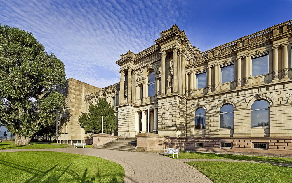 Fachada do Museu Stadel com paredes de pedras claras e um gramado em frente.