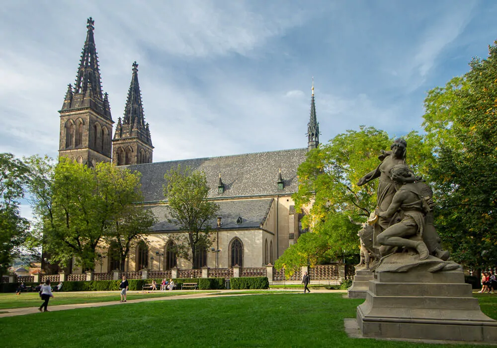 Jardim com gramado, árvores, estátuas e o Castelo de Vyšehrad ao lado.