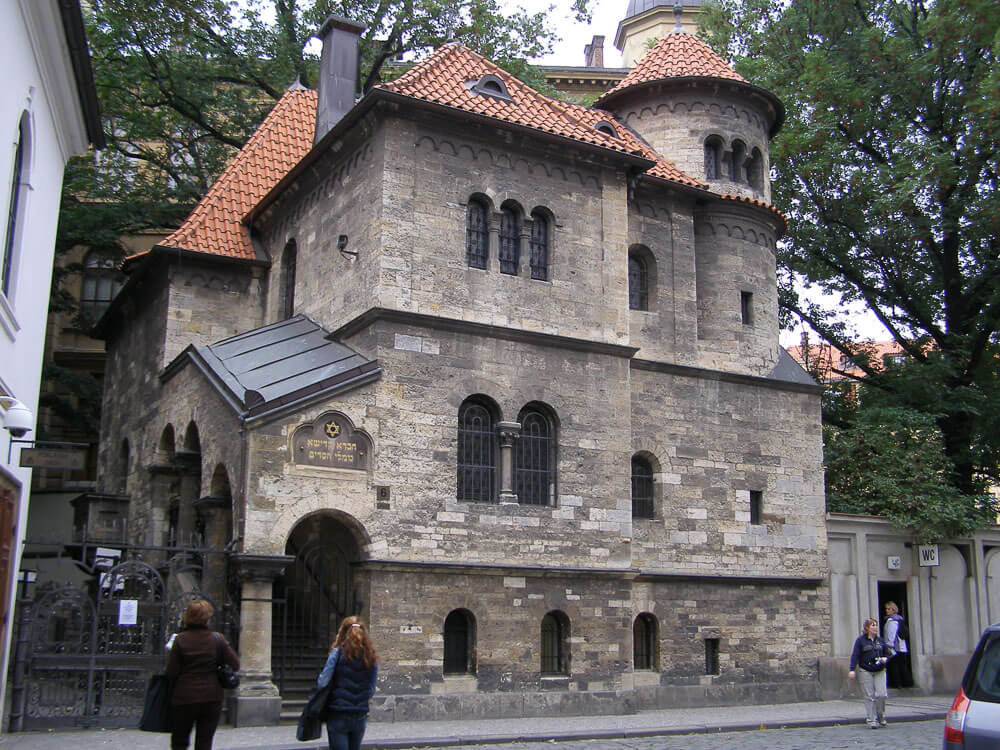 Fachada do Salão Cerimonial de Praga com arquitetura similar a um castelo e com pessoas caminhando na rua em frente ao local.