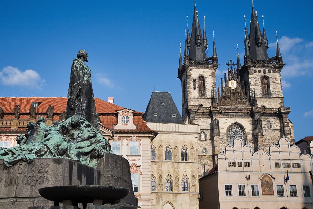 Praça da Cidade Antiga com o monumento Jan Hus à esquerda e prédios históricos à direita.