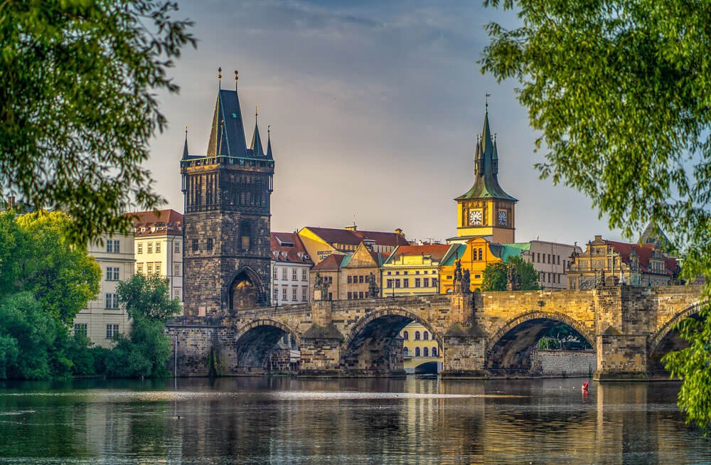 Ponte Carlos sobre as águas escuras do Rio Moldava e, em terra firme, os edifícios históricos de Praga.