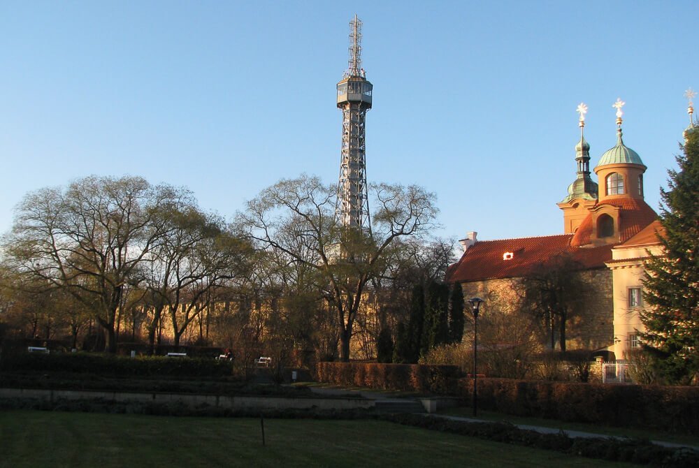Parque Petřín com jardim de aspecto outonal, uma Torre de Observação e um castelo.